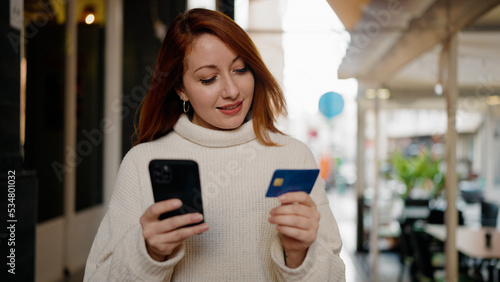 Young redhead woman using smartphone and credit card at street