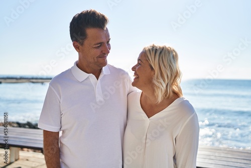 Middle age man and woman couple hugging each other standing at seaside