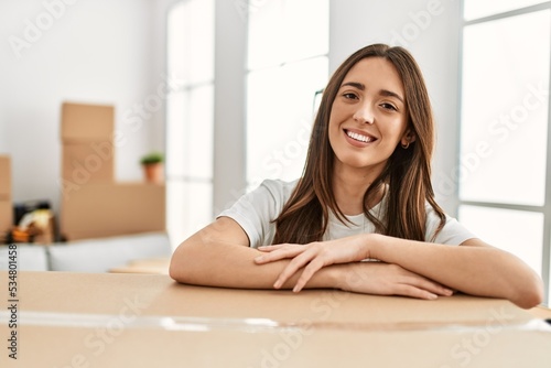 Young hispanic woman smiling confident leaning on package at new home Free Download Young hispanic woman smiling confident leaning on package at new home - GFXLoad