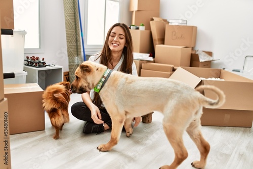 Young hispanic woman smiling confident sitting on floor with dogs at new home