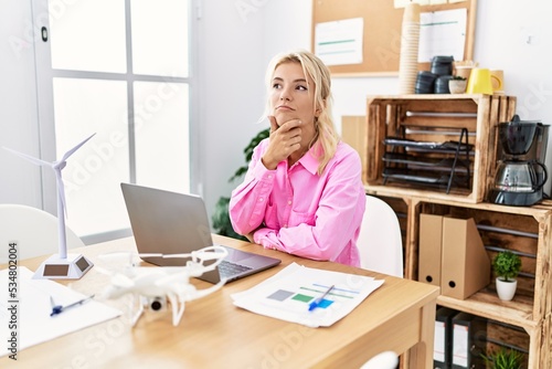 Young caucasian woman working at the office with hand on chin thinking about question, pensive expression. smiling with thoughtful face. doubt concept.
