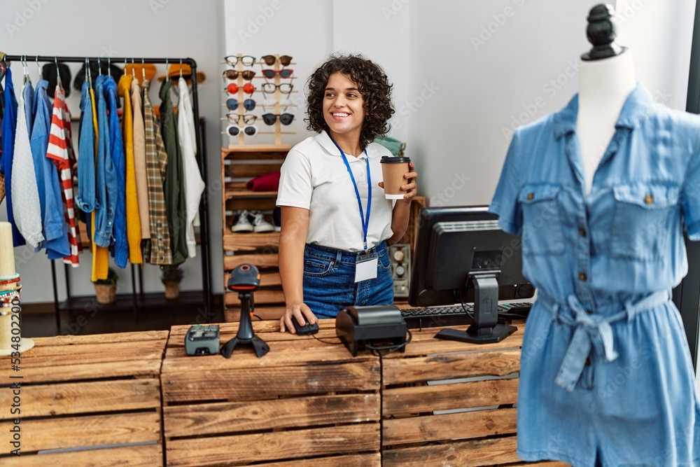 Young latin shopkeeper woman smiling happy working  and drinking coffee at clothing store.