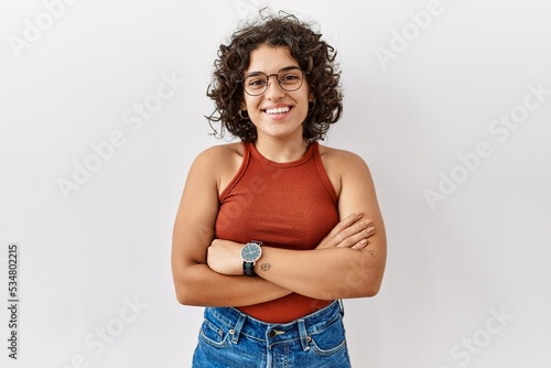 Young hispanic woman wearing glasses standing over isolated background happy face smiling with crossed arms looking at the camera. positive person.