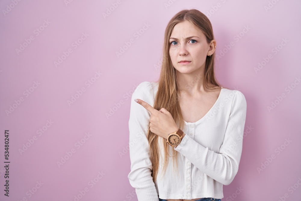 Young caucasian woman standing over pink background pointing aside worried and nervous with forefinger, concerned and surprised expression Young caucasian woman standing over pink background pointing aside worried and nervous with forefinger, concerned and surprised expression