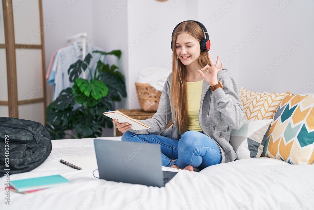 Young caucasian woman studying with laptop sitting on the bed doing ok sign with fingers, smiling friendly gesturing excellent symbol Young caucasian woman studying with laptop sitting on the bed doing ok sign with fingers, smiling friendly gesturing excellent symbol
