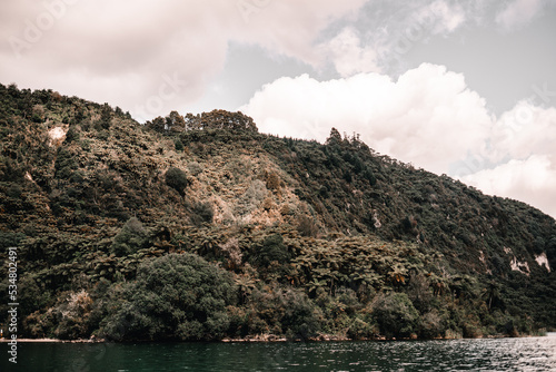 overgrown mountains with lots of trees on the shore of a blue lake under a stormy sky full of white and gray clouds, tarawera lake, new zealand photo