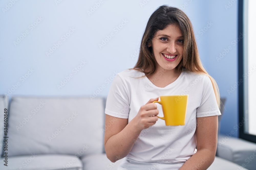 Young hispanic woman drinking coffee sitting on sofa at home Young hispanic woman drinking coffee sitting on sofa at home