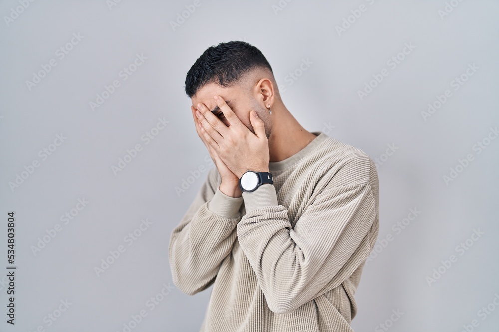 Young handsome man standing over isolated background with sad expression covering face with hands while crying. depression concept. Young handsome man standing over isolated background with sad expression covering face with hands while crying. depression concept.