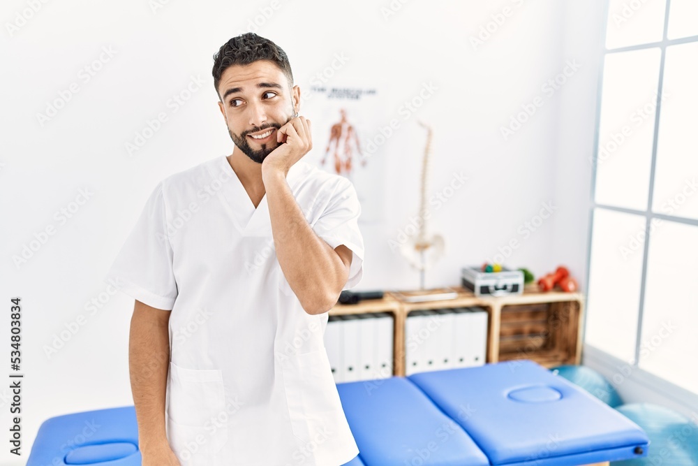 Young handsome man with beard working at pain recovery clinic looking stressed and nervous with hands on mouth biting nails. anxiety problem. Young handsome man with beard working at pain recovery clinic looking stressed and nervous with hands on mouth biting nails. anxiety problem.