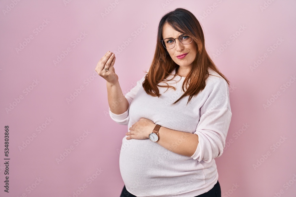 Pregnant woman standing over pink background doing italian gesture with hand and fingers confident expression Pregnant woman standing over pink background doing italian gesture with hand and fingers confident expression