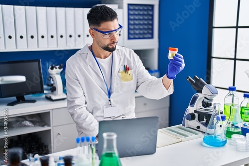 Young arab man scientist using laptop holding urine test tube analysis at laboratory