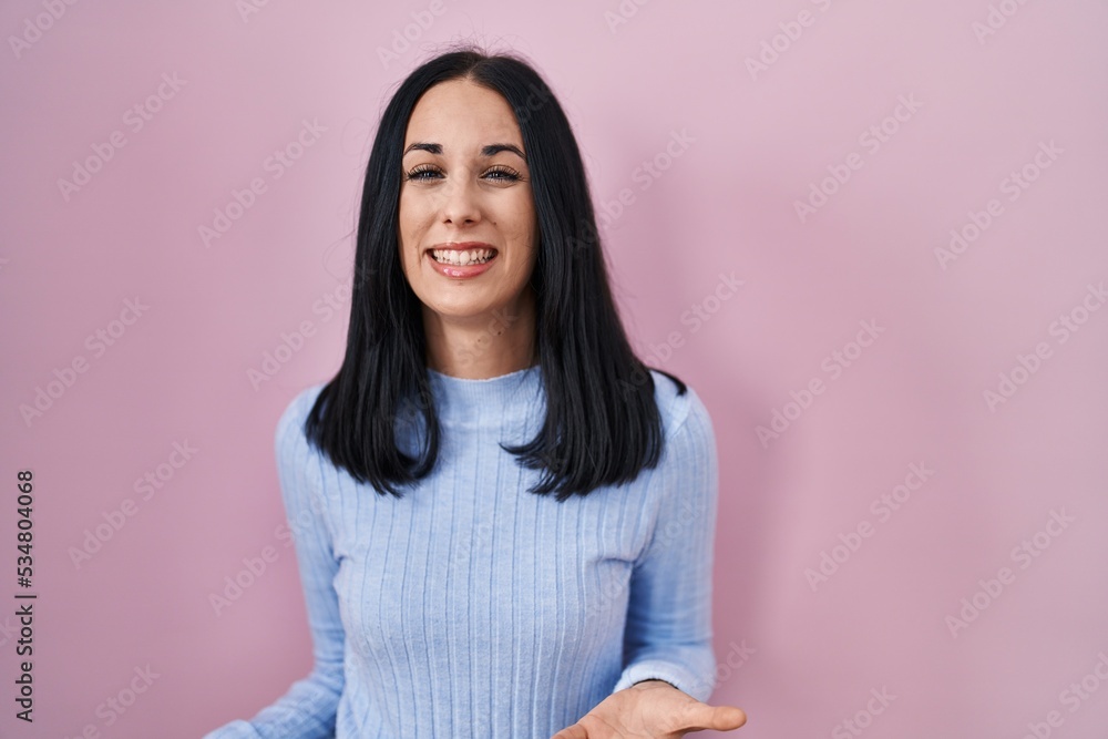 Hispanic woman standing over pink background smiling cheerful with open arms as friendly welcome, positive and confident greetings Hispanic woman standing over pink background smiling cheerful with open arms as friendly welcome, positive and confident greetings