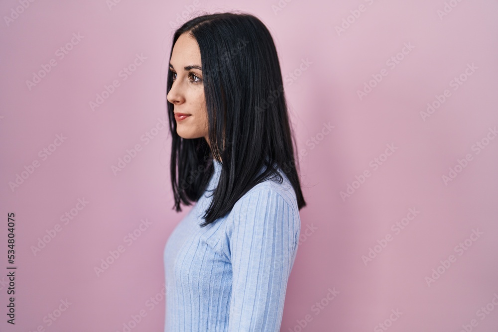 Hispanic woman standing over pink background looking to side, relax profile pose with natural face and confident smile. Hispanic woman standing over pink background looking to side, relax profile pose with natural face and confident smile.