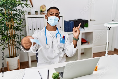 Young indian doctor offering safety mask smiling happy pointing with hand and finger to the side