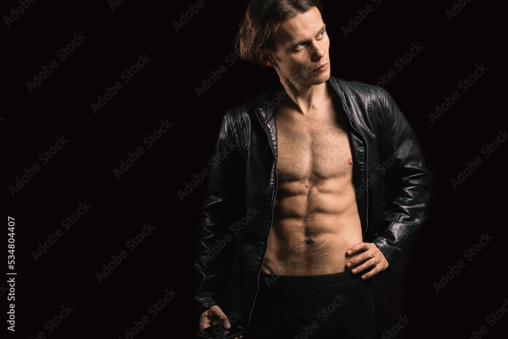 handsome macho man with a naked torso in a black leather jacket on a dark background.