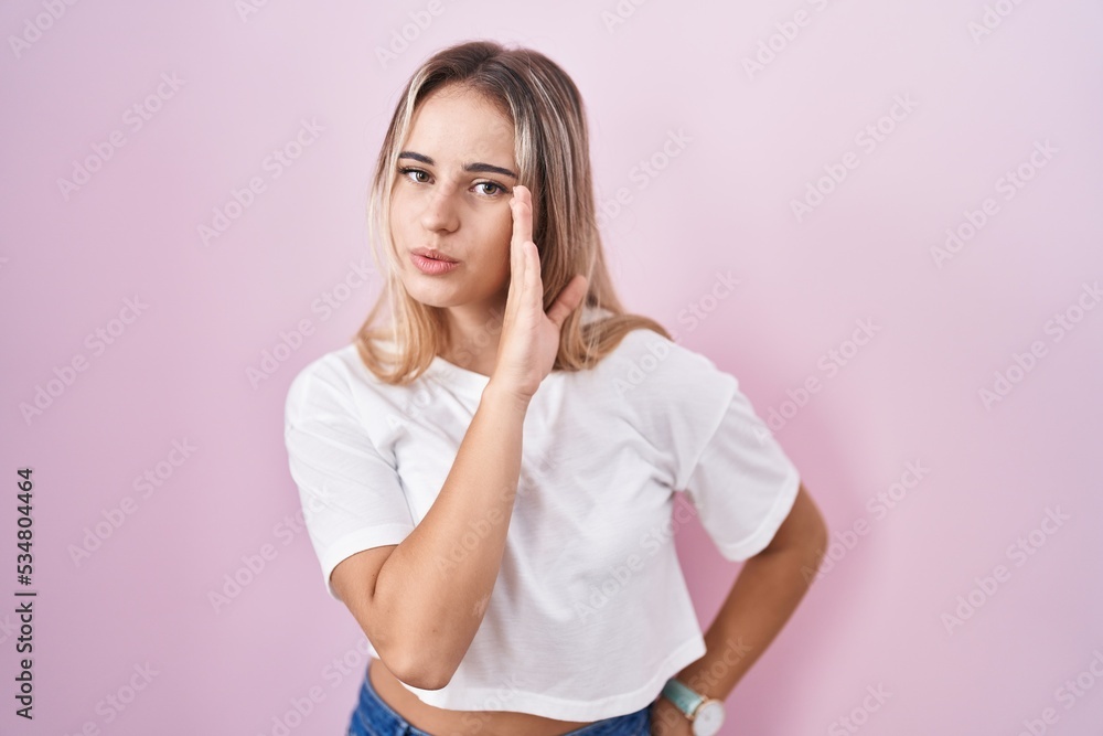 Young blonde woman standing over pink background hand on mouth telling secret rumor, whispering malicious talk conversation Young blonde woman standing over pink background hand on mouth telling secret rumor, whispering malicious talk conversation