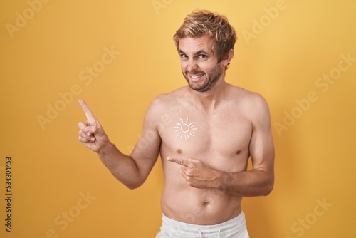 Caucasian man standing shirtless wearing sun screen pointing aside worried and nervous with both hands  concerned and surprised expression