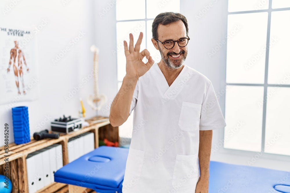 Middle age man with beard working at pain recovery clinic smiling positive doing ok sign with hand and fingers. successful expression. Middle age man with beard working at pain recovery clinic smiling positive doing ok sign with hand and fingers. successful expression.