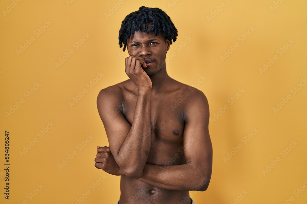 Fototapeta premium Young african man with dreadlocks standing shirtless looking stressed and nervous with hands on mouth biting nails. anxiety problem.