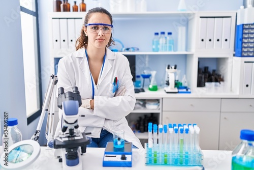 Young hispanic woman working at scientist laboratory skeptic and nervous  disapproving expression on face with crossed arms. negative person.