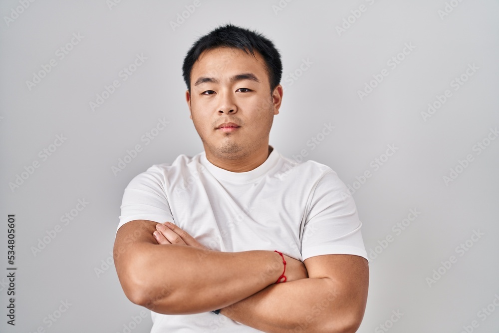 Young chinese man standing over white background skeptic and nervous, disapproving expression on face with crossed arms. negative person. Young chinese man standing over white background skeptic and nervous, disapproving expression on face with crossed arms. negative person.