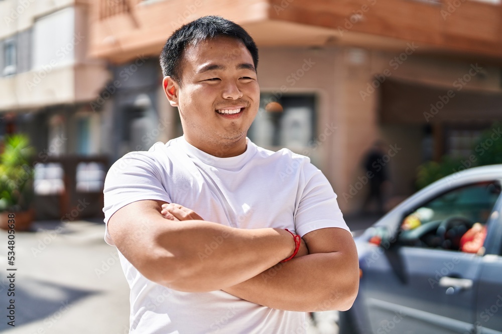 Young chinese man smiling confident standing with arms crossed gesture at street