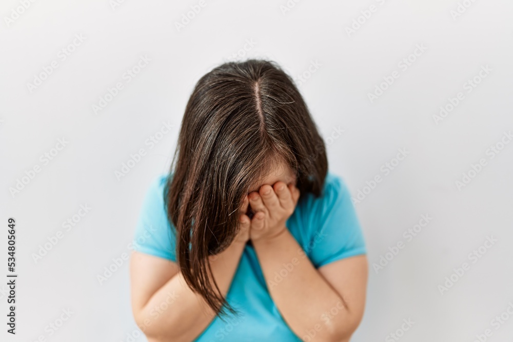 Young down syndrome woman standing over isolated background with sad expression covering face with hands while crying. depression concept. Young down syndrome woman standing over isolated background with sad expression covering face with hands while crying. depression concept.