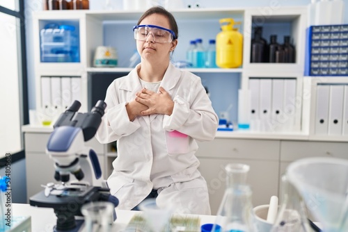 Hispanic girl with down syndrome working at scientist laboratory smiling with hands on chest with closed eyes and grateful gesture on face. health concept.
