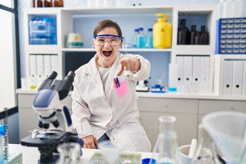 Hispanic girl with down syndrome working at scientist laboratory pointing displeased and frustrated to the camera, angry and furious with you