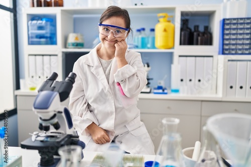 Hispanic girl with down syndrome working at scientist laboratory looking stressed and nervous with hands on mouth biting nails. anxiety problem.