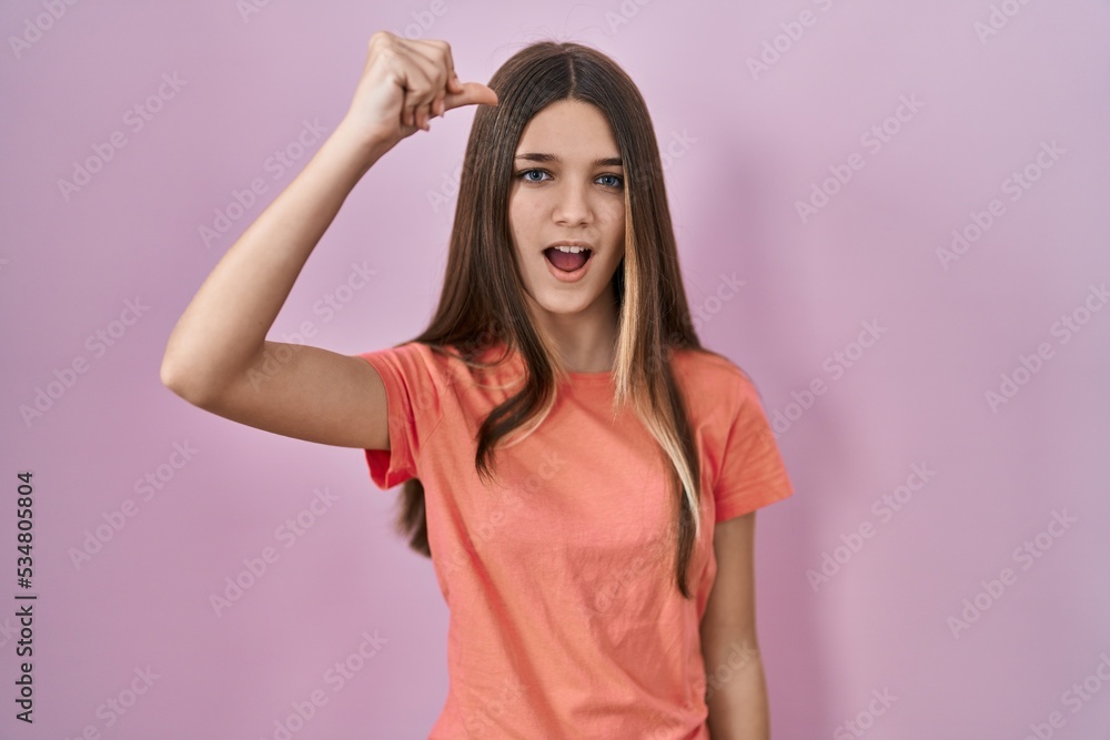 Teenager girl standing over pink background angry and mad raising fist frustrated and furious while shouting with anger. rage and aggressive concept.