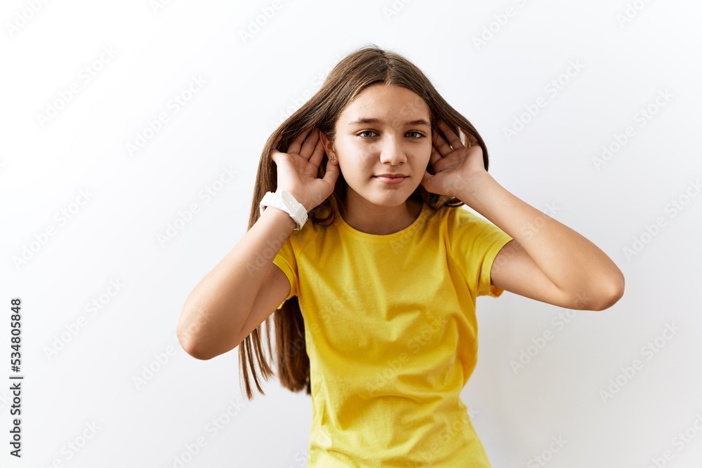 Young brunette teenager standing together over isolated background trying to hear both hands on ear gesture, curious for gossip. hearing problem, deaf Young brunette teenager standing together over isolated background trying to hear both hands on ear gesture, curious for gossip. hearing problem, deaf