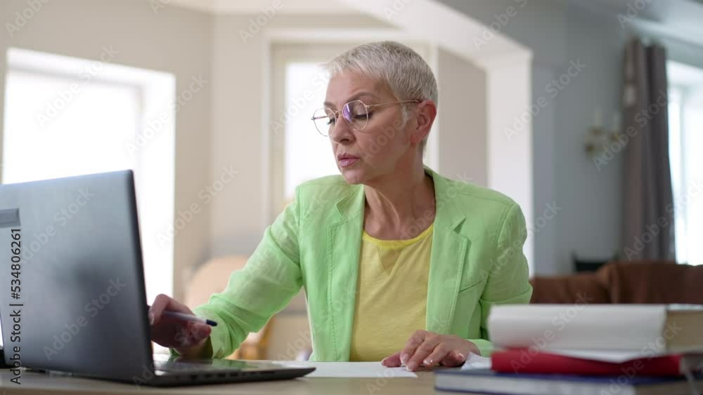 Portrait of busy middle aged businesswoman surfing Internet on laptop writing with pen sneezing in slow motion. Concentrated Caucasian woman messaging online working in home office Portrait of busy middle aged businesswoman surfing Internet on laptop writing with pen sneezing in slow motion. Concentrated Caucasian woman messaging online working in home office