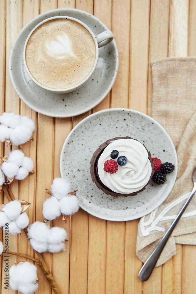 Tender french cupcake with cup of coffee outside. Atmospheric cotton decoration. Cozy breakfast at the terrace, guilty pleasure Tender french cupcake with cup of coffee outside. Atmospheric cotton decoration. Cozy breakfast at the terrace, guilty pleasure