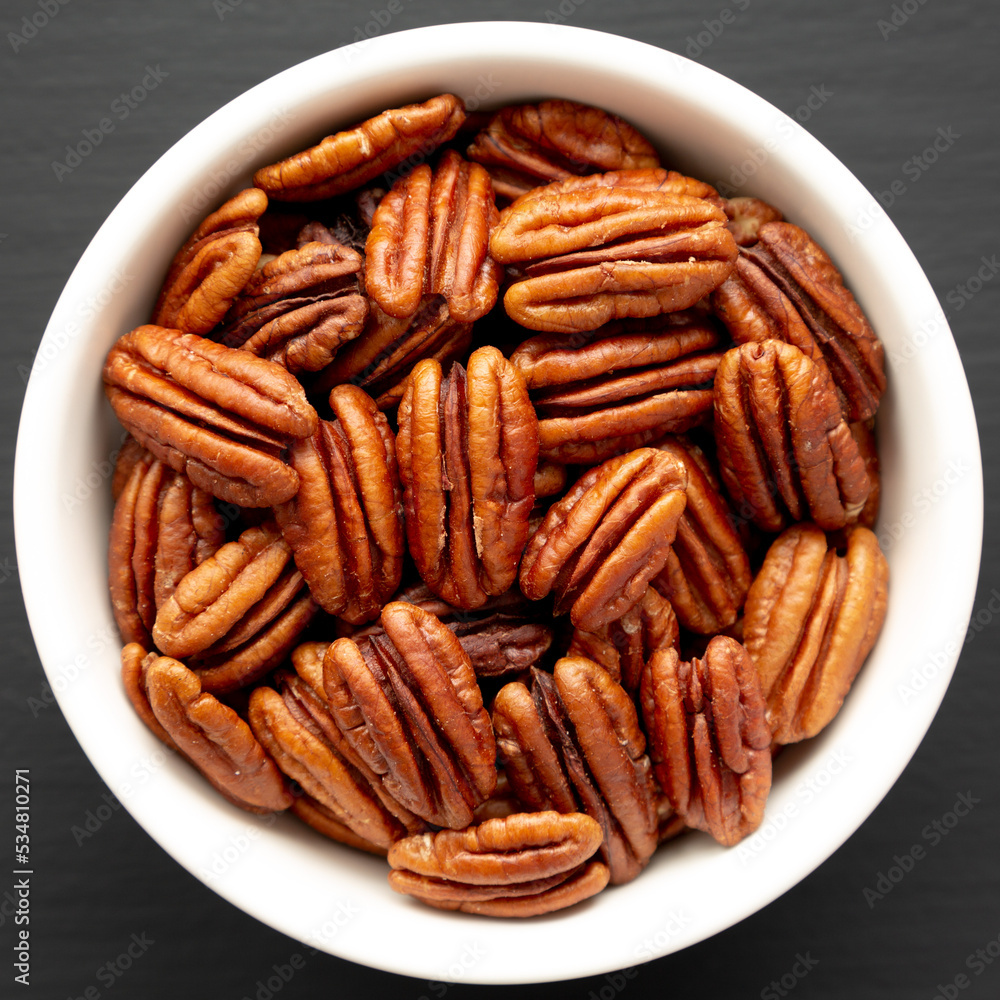 Homemade Shelled Pecans in a bowl on a black background, top view. Flat lay, overhead, from above. Homemade Shelled Pecans in a bowl on a black background, top view. Flat lay, overhead, from above.