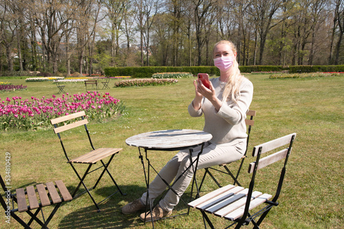 young woman in a protective mask takes a selfie with blooming sprimg tulips photo