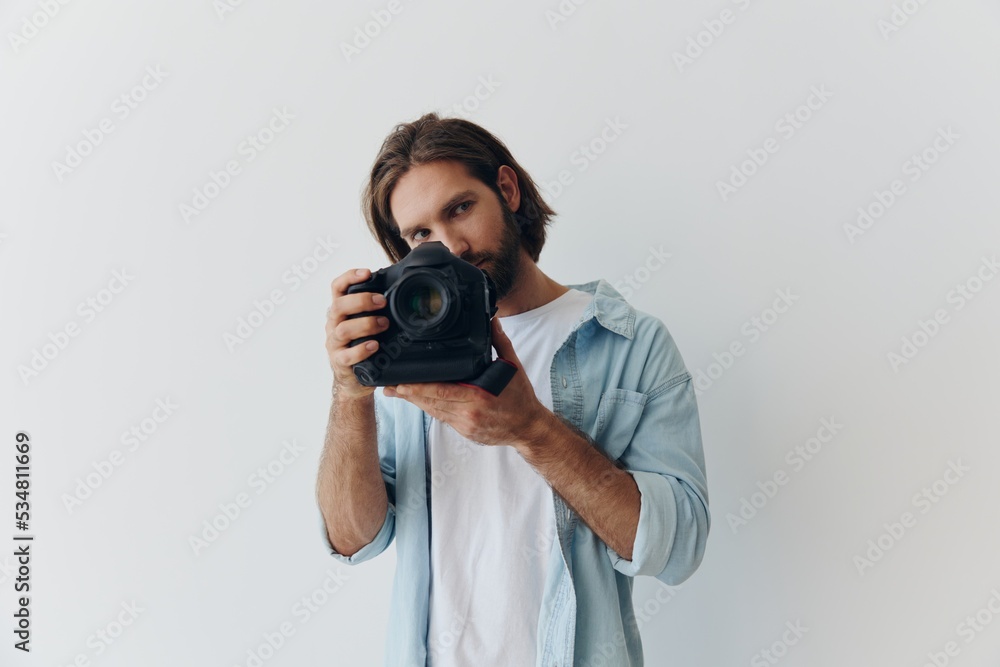 Man hipster photographer in a studio against a white background holding a professional camera and setting it up before shooting. Lifestyle work as a freelance photographer