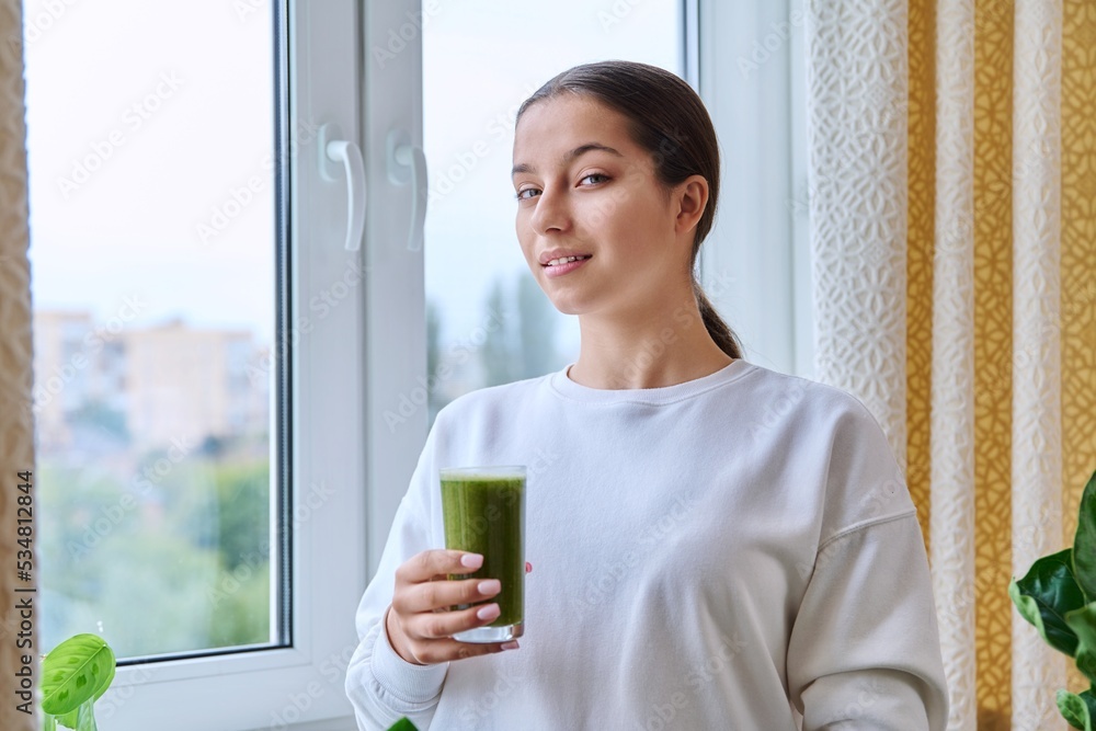Teenage girl with glass of green fresh in morning at home near window Teenage girl with glass of green fresh in morning at home near window
