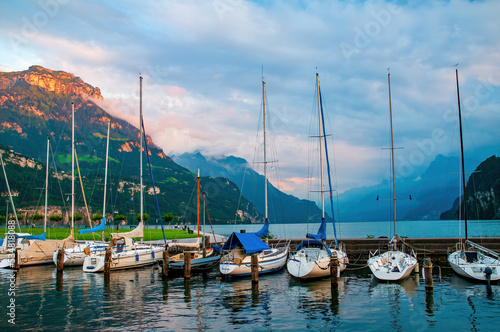 Yachts moored to the pier on Lucerne Lake  Brunnen  Canton of Schwyz  Switzerland. Mountains illuminated by sunset on background. Brunnen is a popular resort on Vierwaldstattersee