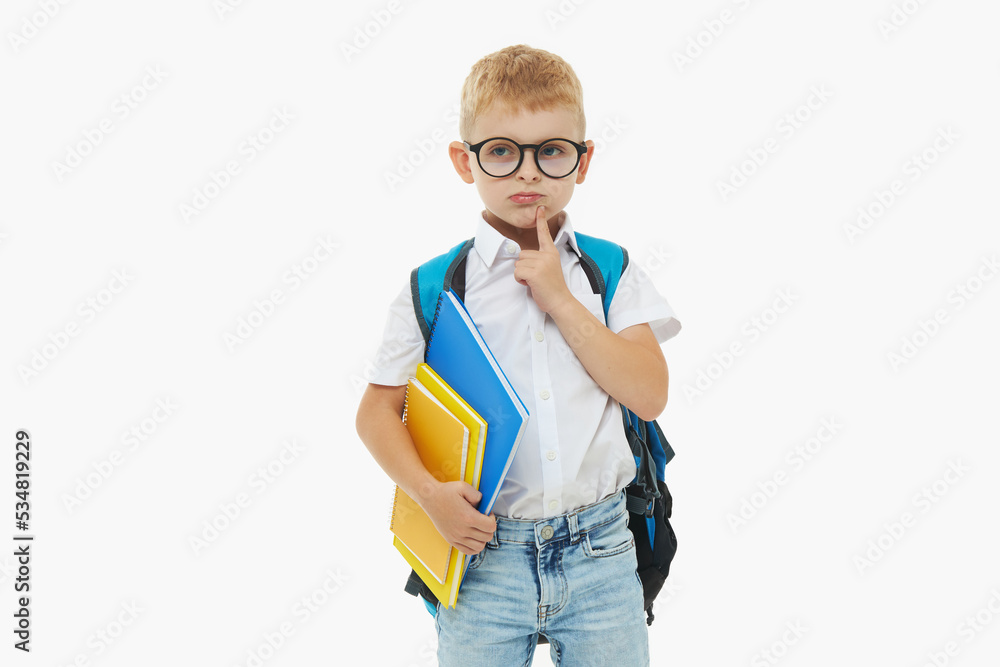 Back to school. Funny little boy from elementary school with a book, a backpack and glasses on a white background. Laughs merrily. Preparation for school. Concept of early development Back to school. Funny little boy from elementary school with a book, a backpack and glasses on a white background. Laughs merrily. Preparation for school. Concept of early development