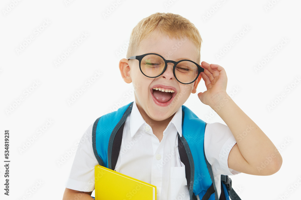 Back to school. Funny little boy from elementary school with a book, a backpack and glasses on a white background. Laughs merrily. Preparation for school. Concept of early development Back to school. Funny little boy from elementary school with a book, a backpack and glasses on a white background. Laughs merrily. Preparation for school. Concept of early development