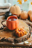 A cup of tea in the shape of a pumpkin against the background of stacks of sweaters, autumn mood