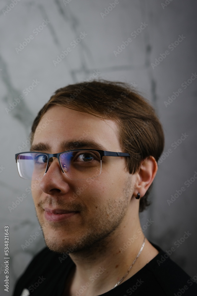 Unshorn and unshaven guy in glasses and black tshirt with long hair on gray background Unshorn and unshaven guy in glasses and black tshirt with long hair on gray background