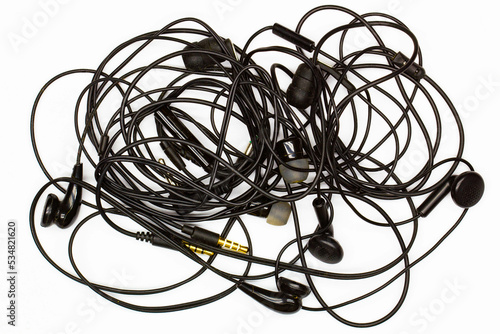 Old tangled headphones on a white background. Isolated. Black dusty dirty wired headphones with tangled wires. Audio Speakers, microphones, plugs and volume controls. Built-in vacuum music headset.