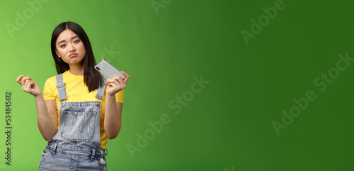 Bored indifferent cool urban asian girl waste time summer holiday alone, playing smartphone game, interrupt texting, browsing internet, gesturing reluctant, look sad, losing battle, green background