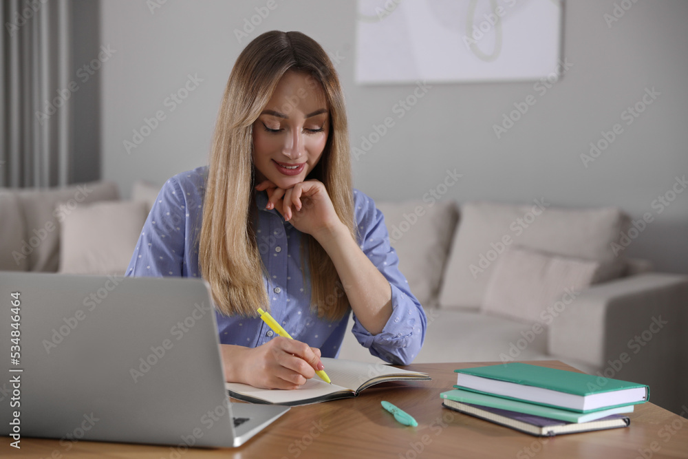 Young woman writing down notes during webinar at table in room Young woman writing down notes during webinar at table in room