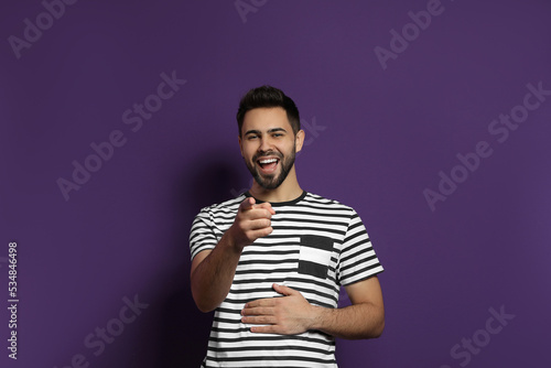 Young man laughing on purple background. Funny joke