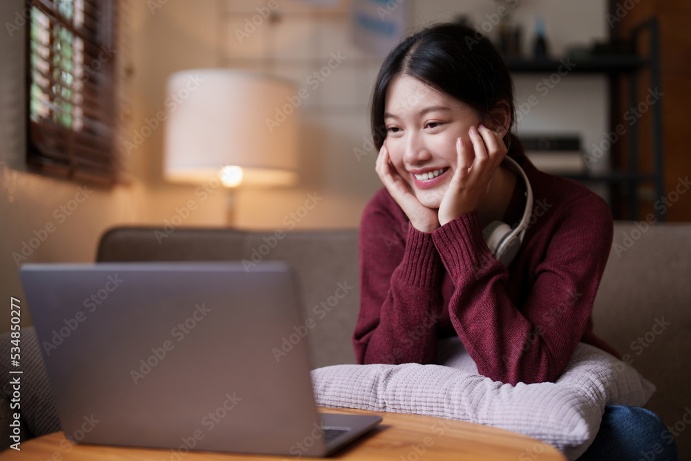Young asian woman sitting on couch looking at laptop in cozy living room at home. Lifestyle concept Young asian woman sitting on couch looking at laptop in cozy living room at home. Lifestyle concept