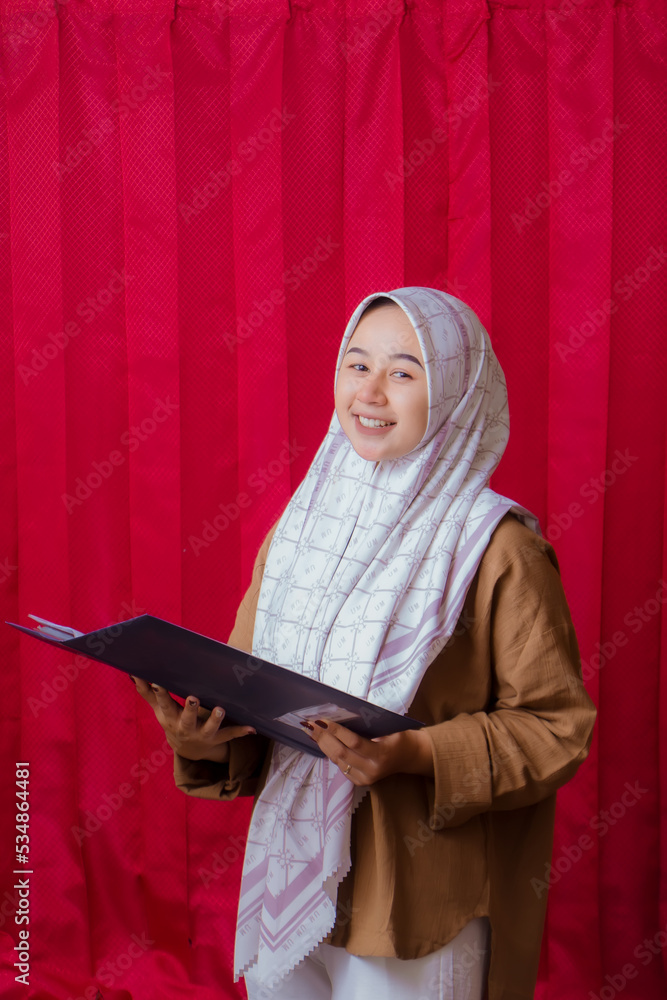 Portrait of cheerful beautiful Asian Woman in casual shirt. Beautiful Muslim Girl. Beautiful asian muslim female model posing in studio on red background. Portrait of cheerful beautiful Asian Woman in casual shirt. Beautiful Muslim Girl. Beautiful asian muslim female model posing in studio on red background.
