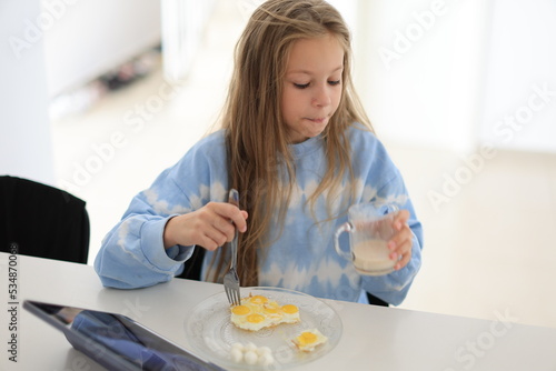 little girl drinks whole cow's milk with egg in the morning sitting at the table. The child enjoys a healthy natural drink while having breakfast in kitchen at home. Proper nutrition for children